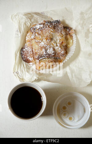 Francese croissant al cioccolato e un bicchiere di carta di caffè su un tavolo bianco Foto Stock