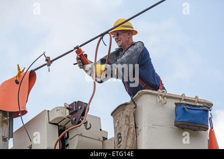 Lineman utilizza un elevato della piattaforma di lavoro denominato 'cherry picker' per riparare le linee elettriche in alto su un polo utilità. Foto Stock