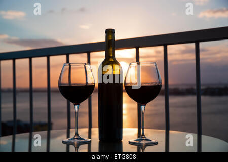 Silhouette della bottiglia e bicchieri di vino rosso nel tramonto con vista mare sullo sfondo Foto Stock
