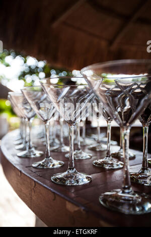 Svuotare bicchieri da Martini impostazione in fila, fuori sulla barra di legno contatore a erba tropicale palapa, pronto per feste, sele Foto Stock