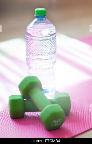 Due manubri con acqua minerale sul materassino yoga contro la luce solare, profondità. È molto importante bere acqua a allenamento Foto Stock