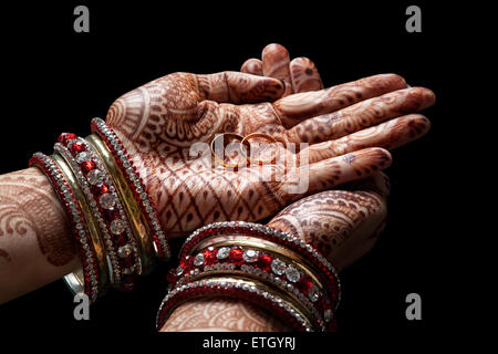 Donna mani con henna tenendo due golden gli anelli di nozze su sfondo nero Foto Stock