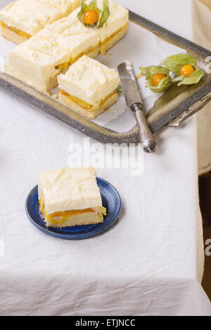 In casa fette di torta con mousse cremosa e frutti tropicali di mango e physalis servita nel vintage vassoio di metallo su tavolo bianco. Se Foto Stock