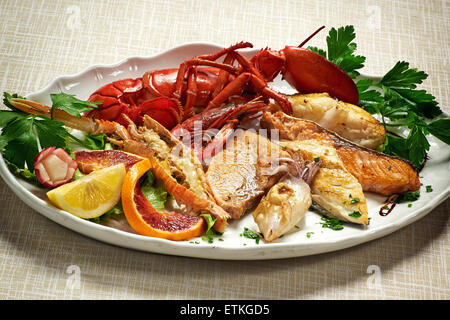 Close up gourmet gustosa grigliata mista di pesce e di aragosta ricetta servita su piastra bianca con il coriandolo erbe messi sul tavolo. Foto Stock