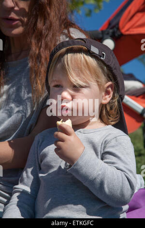 Ritratto di due anni di età bambino biondo con cappuccio nero mangiare banana accanto alla donna madre Foto Stock