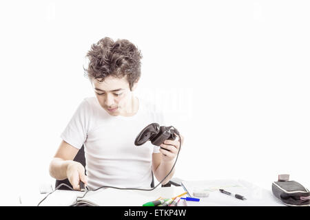 Ragazzo caucasica nel manicotto corto t-shirt gioca con un controller di gioco seduti di fronte la sua casa sulla scrivania Foto Stock