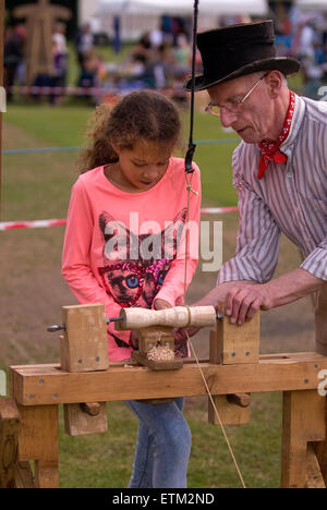 Artigiano di dimostrare alla giovane ragazza l'artigianato del legno cime di filatura a Churt Fete, Churt Ricreazione Terra, Churt... Foto Stock