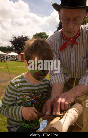 Artigiano dimostrando al giovane ragazzo l'artigianato del legno cime di filatura a Churt Fete, Churt, Farnham, Surrey, Regno Unito. Foto Stock