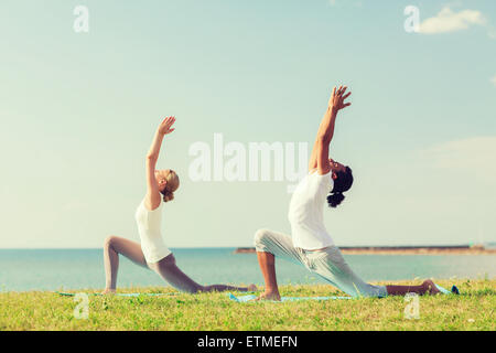 Coppia sorridente facendo esercizi di yoga all'aperto Foto Stock