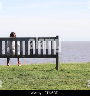 Ragazza seduta sul banco di lavoro guardando al mare Foto Stock