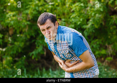 Uomo di strada dolore addominale su uno sfondo verde foglie Foto Stock