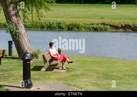 Signora seduti sulla panca sulla giornata di sole oltre il fiume Ouse, grande Barford, Bedfordshire, Inghilterra Foto Stock