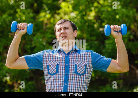 L'uomo della strada tenendo una plastica manubri sport su un blu Foto Stock