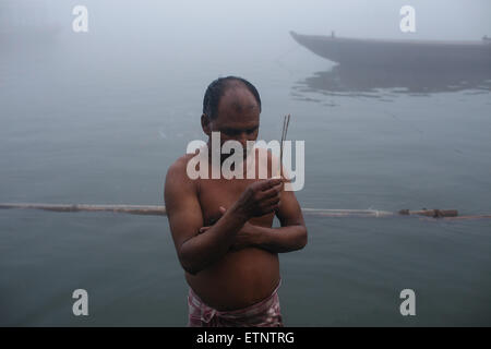 Un uomo pellegrino in preghiera nella foschia mattutina nel fiume Gange a ghats di Varanasi, India Foto Stock