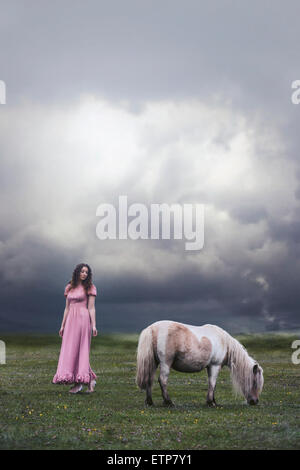 Una ragazza in un abito rosa è in piedi su un paddock con un pony Foto Stock