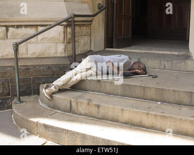 Uomo con una canna dorme sui gradini di una chiesa cristiana lungo la 7th Avenue a Park Slope, Brooklyn, New York. Foto Stock