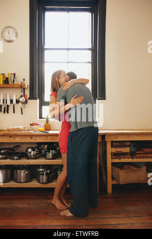 Felice giovane donna essendo abbracciato con il suo fidanzato in cucina. Allegro coppia giovane che abbraccia ogni altra in mattinata a casa. Foto Stock