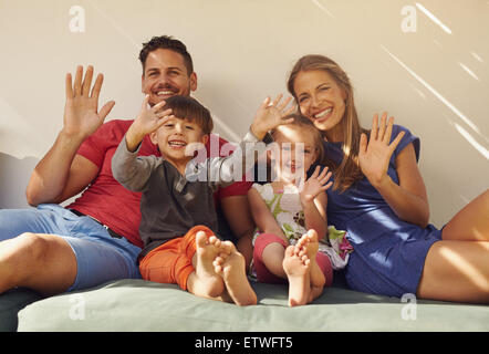 Famiglia seduti sul divano a sorridere e ridere insieme, sventolando in telecamera. Coppia con bambini sul patio avendo divertimento all'aperto in loro Foto Stock