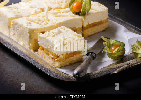 In casa fette di torta con mousse cremosa e frutti tropicali di mango e physalis servita nel vintage vassoio di metallo su backgroun nero Foto Stock