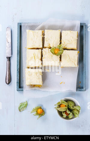 In casa fette di torta con mousse cremosa e frutti tropicali di mango e physalis servita nel vassoio in legno su fondo azzurro. Foto Stock