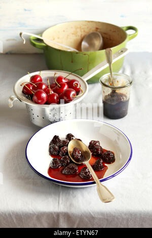 Confettura di ciliegie su una piastra,ciliegia fresca in alluminio scolapasta e dutch pot con marmellata di ciliege sullo sfondo Foto Stock