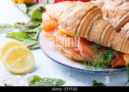 Croissant sandwich con salmone salato sulla piastra bianca, servito con insalata fresca foglie di limone, il sale di mare e le verdure sopra la luce Foto Stock