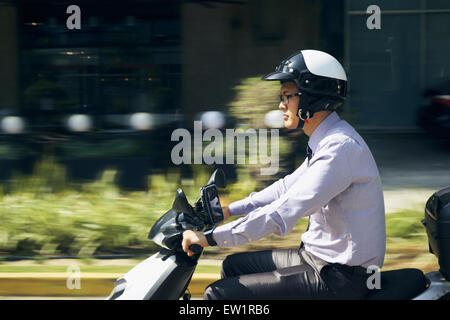 Giovane imprenditore asiatico il pendolarismo per lavoro. L'uomo cavalca un motociclo con casco bianco. Motion sfondo sfocato Foto Stock