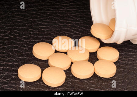 Tablet medications fuoriuscita da una bottiglia di plastica bianca che scorre sul marrone medici in similpelle desk. Foto Stock