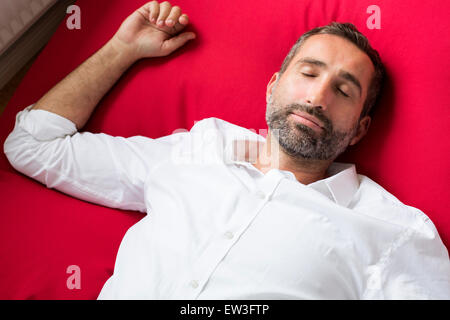 Ritratto di un Uomo in camicia bianca giacente su un cuscino rosso e il sonno Foto Stock