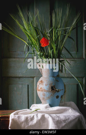 Bouquet di yang orzo verde con la fioritura del papavero rosso fiore nel vecchio vaso di metallo su un tavolo di legno. Dark atmosfera rustica Foto Stock