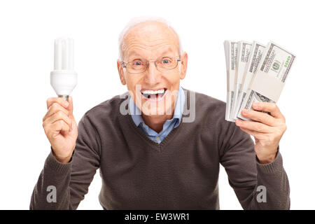 Felice senior gentleman tenendo un risparmio energetico lampadina e quattro pile di denaro isolato su sfondo bianco Foto Stock