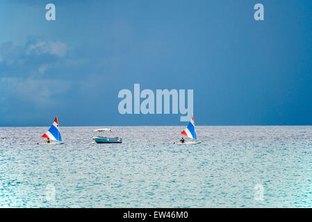 Due piccole barche a vela vela un passato ancorato con una barca a motore ai Caraibi, con cielo tempestoso. Foto Stock