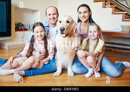 Famiglia amichevole con il cane seduto sul pavimento e guardando la fotocamera Foto Stock