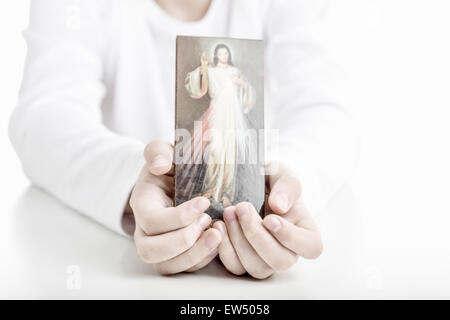 Un ragazzo ispanico mostra una immagine di Gesù Misericordioso tenendolo con entrambe le mani Foto Stock