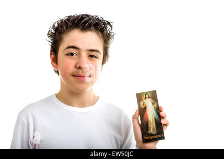 Un felice ragazzo ispanico sorrisi tenendo un immagine in legno di Gesù misericordioso con la mano sinistra Foto Stock