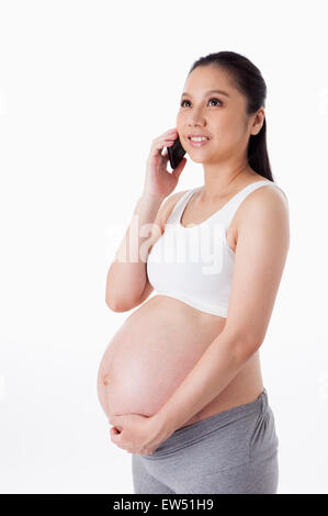 Donna incinta guardando verso l'alto e tenere il telefono cellulare con il sorriso, Foto Stock