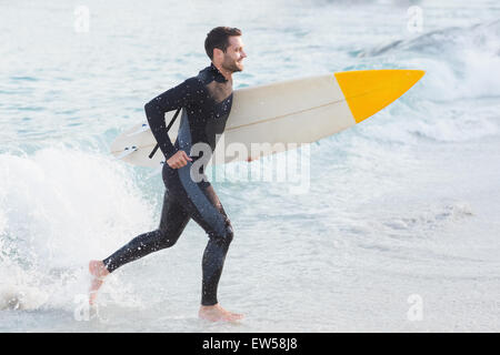 Uomo in neoprene con una tavola da surf in una giornata di sole Foto Stock