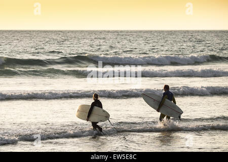 Due surfisti a piedi al mare come il sole tramonta su Fistral Beach in Cornovaglia. Regno Unito. Foto Stock