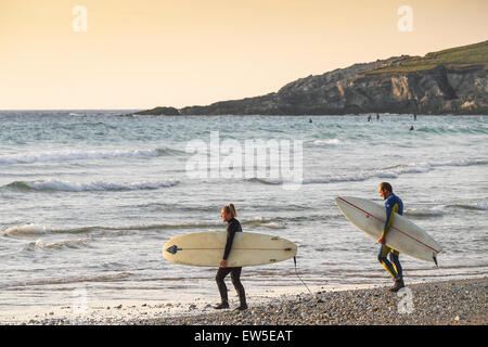 Due surfisti a piedi nel mare come il sole tramonta su Fistral Beach in Newquay, Cornwall. Regno Unito. Foto Stock