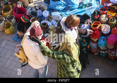 Donna locale venditore di cappelli ottiene un turista a provare sulla sua merci, tra artigianato e souvenir prodotti per la vendita in questo squar Foto Stock