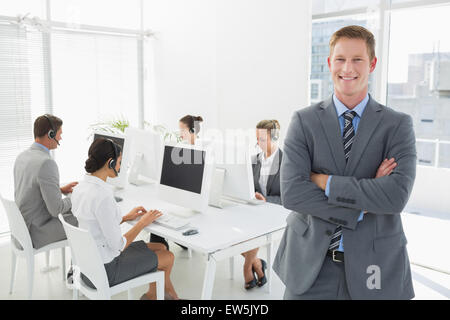 Sorridente manager in piedi con le braccia incrociate con personale dietro Foto Stock