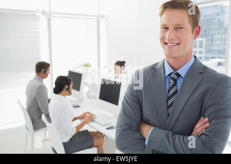 Sorridente manager in piedi con le braccia incrociate con personale dietro Foto Stock