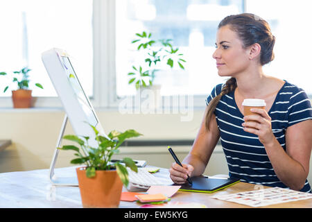Sorridente casual imprenditrice lavorando sul digitalizzatore e tenendo il caffè Foto Stock
