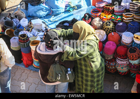 Donna locale venditore di cappelli ottiene un turista a provare sulla sua merci, tra artigianato e souvenir prodotti per la vendita in questo squar Foto Stock