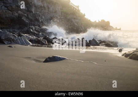 La luce del tramonto su schizzi d'onda sui rocciosi sabbia nera vulcanica beach, Tenerife, Isole Canarie Foto Stock