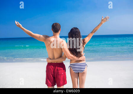 Vista posteriore della coppia felice con le braccia aperte in spiaggia Foto Stock