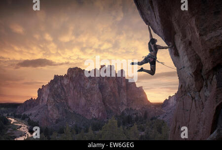 Una femmina di scalatore getta un dyno fino in aria che si affaccia Smith Rock al tramonto. Foto Stock