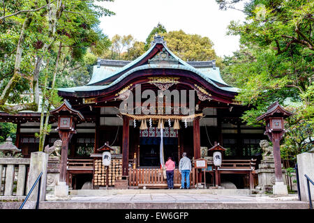 Tempio di Okazaki a Kyoto. Sala principale con stunt shimenawa e corda a campana appesa. Due persone in piedi di fronte pregando fiancheggiata da lanterne di legno. Foto Stock