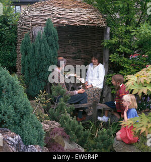 Famiglia seduto accanto a arbor di vimini in giardino Foto Stock