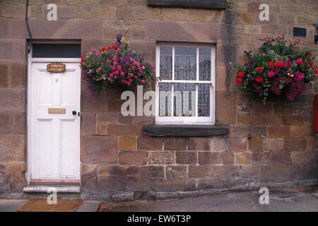 Esterno del cottage con bianco dello sportello anteriore e l'estate annuari in cestelli appesi Foto Stock